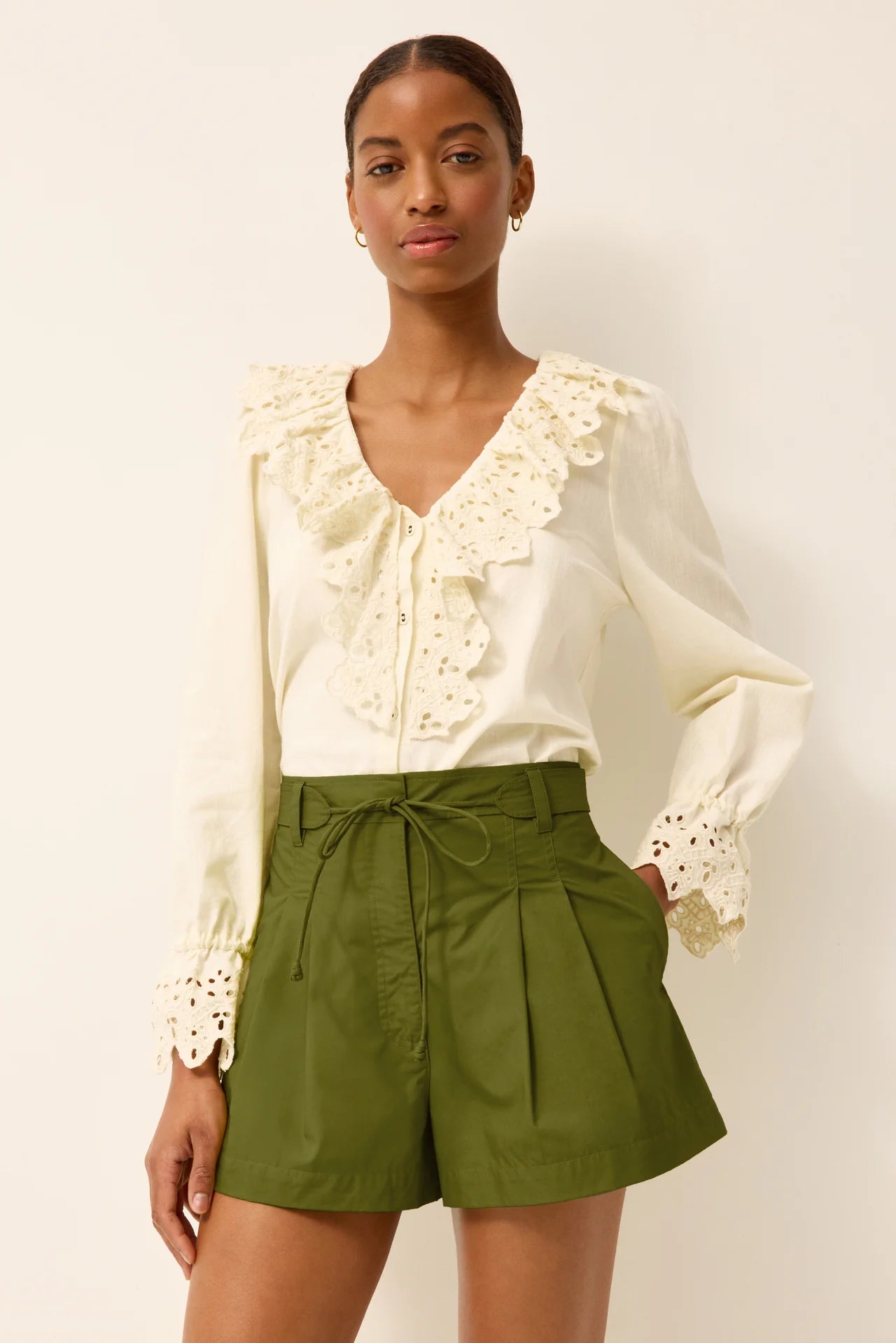 Woman wearing a white blouse with lace details and green shorts on a plain background
