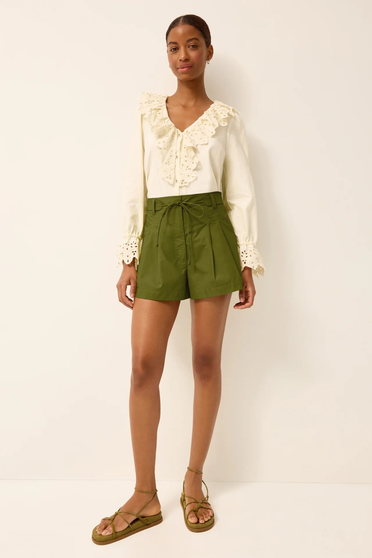 Woman wearing a white blouse with ruffled details and green shorts on a plain background