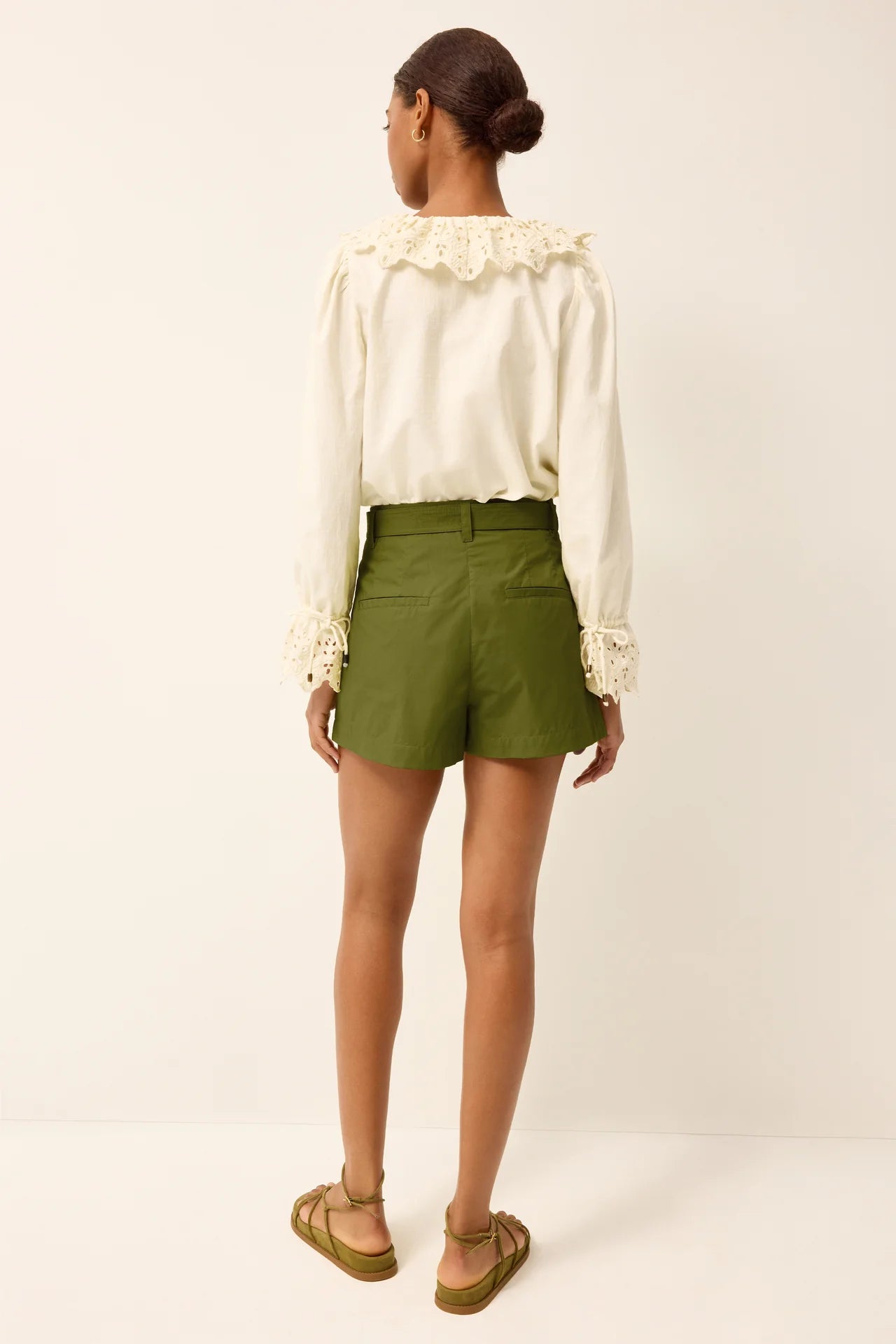 Woman wearing a white blouse with lace details and green shorts on a white background