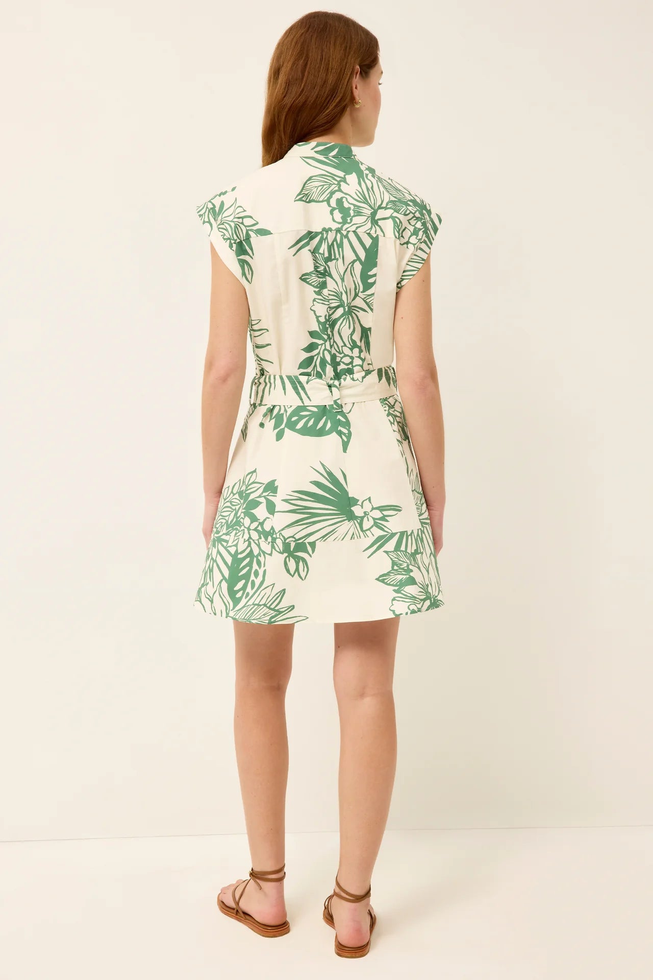 Woman wearing a white dress with green leaf pattern on a plain background