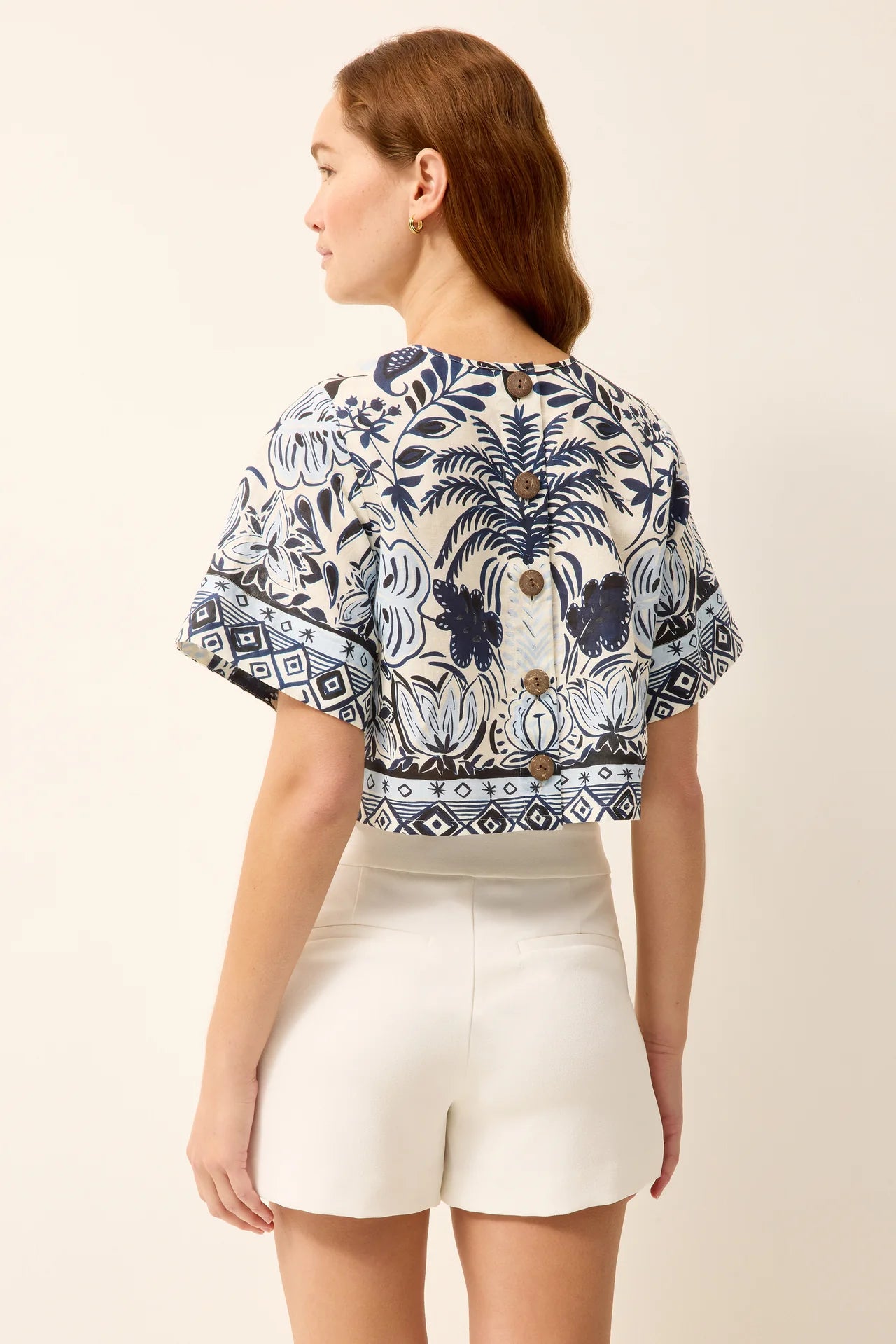 Woman wearing a patterned top and white shorts on a beige background