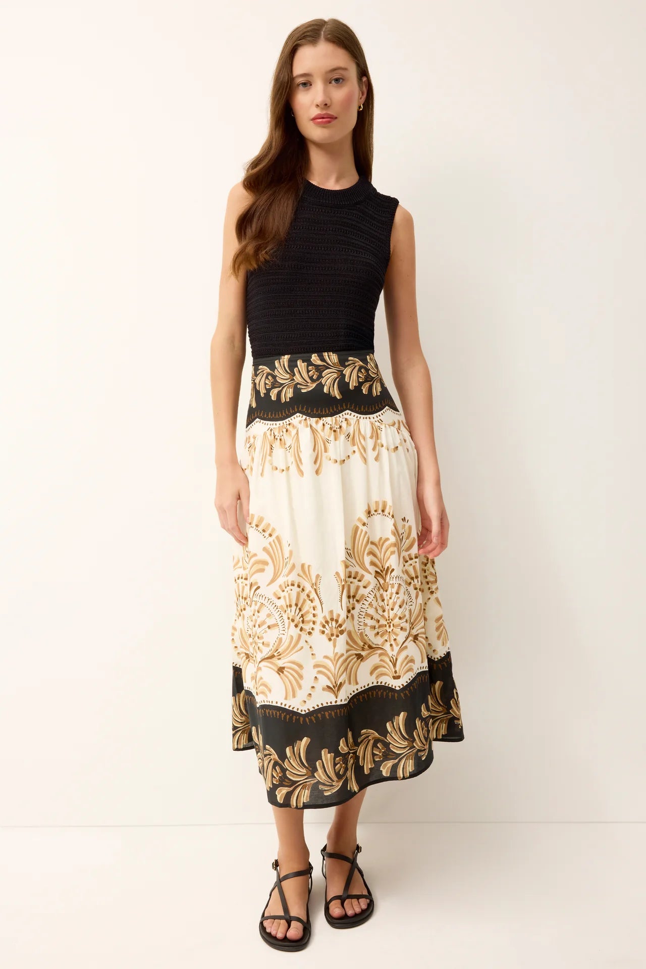 Woman wearing a black top and white skirt with gold patterns on a white background