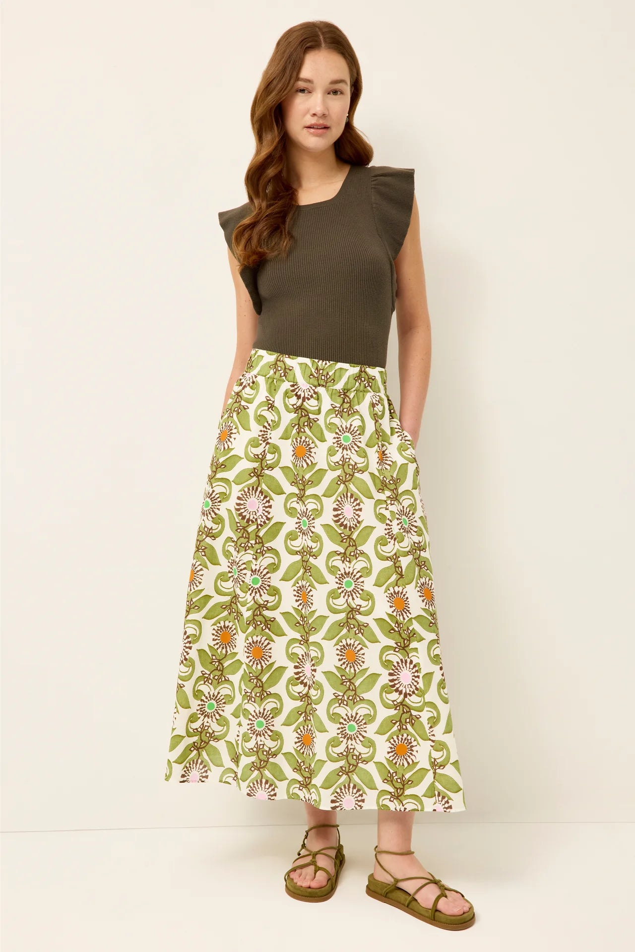 Woman wearing a green patterned skirt and brown top against a white background