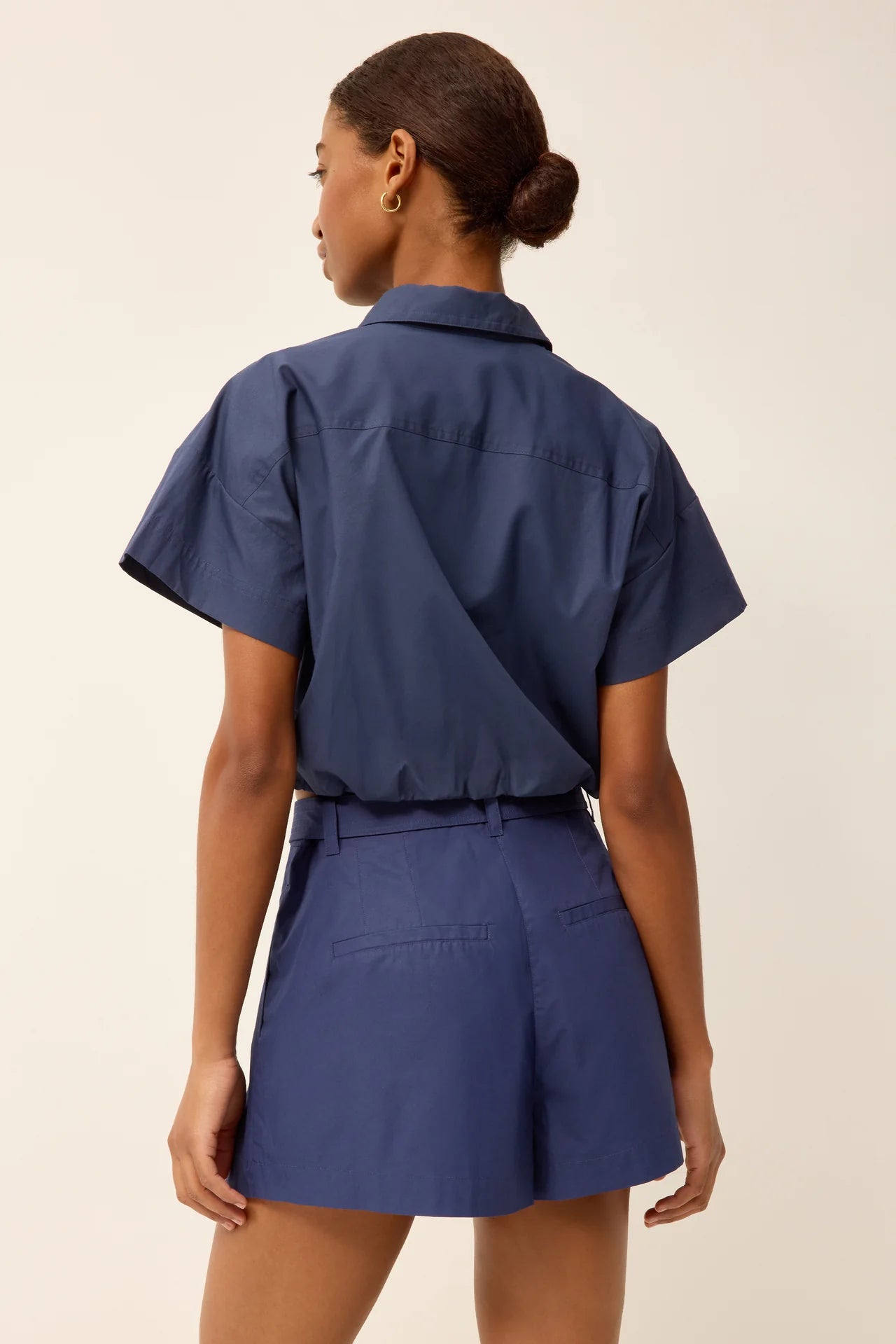 Woman wearing a blue outfit with a belt on a beige background