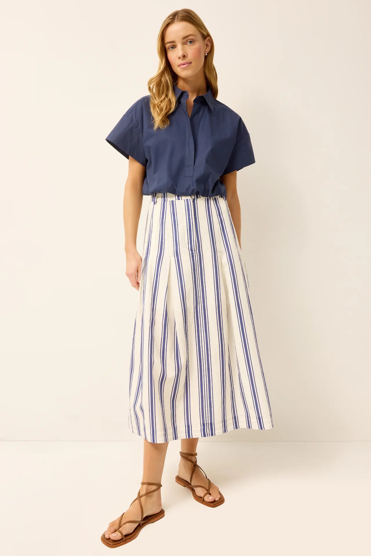 Woman wearing a navy shirt and striped skirt on a plain background