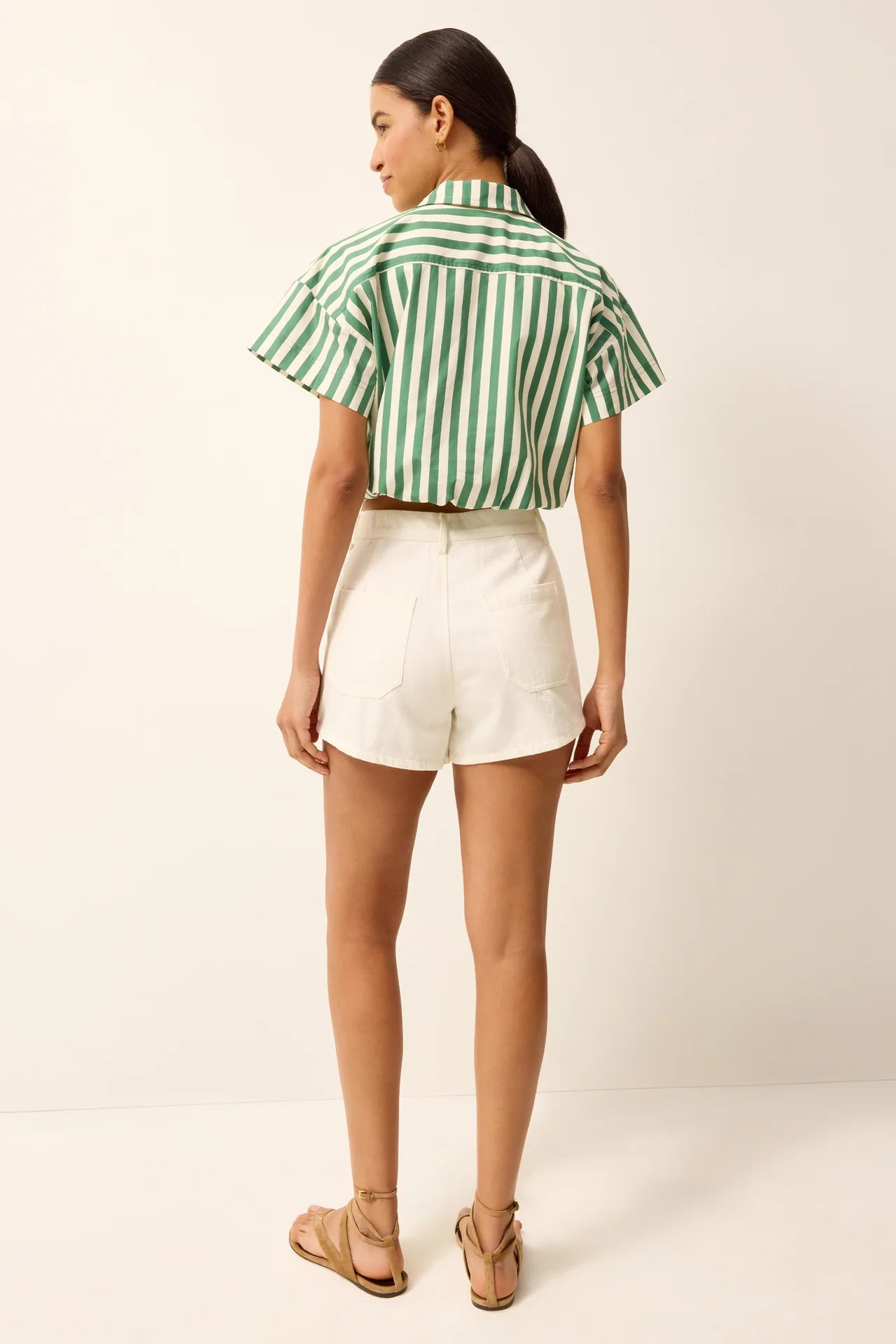 Woman wearing a green and white striped shirt and white shorts on a plain background