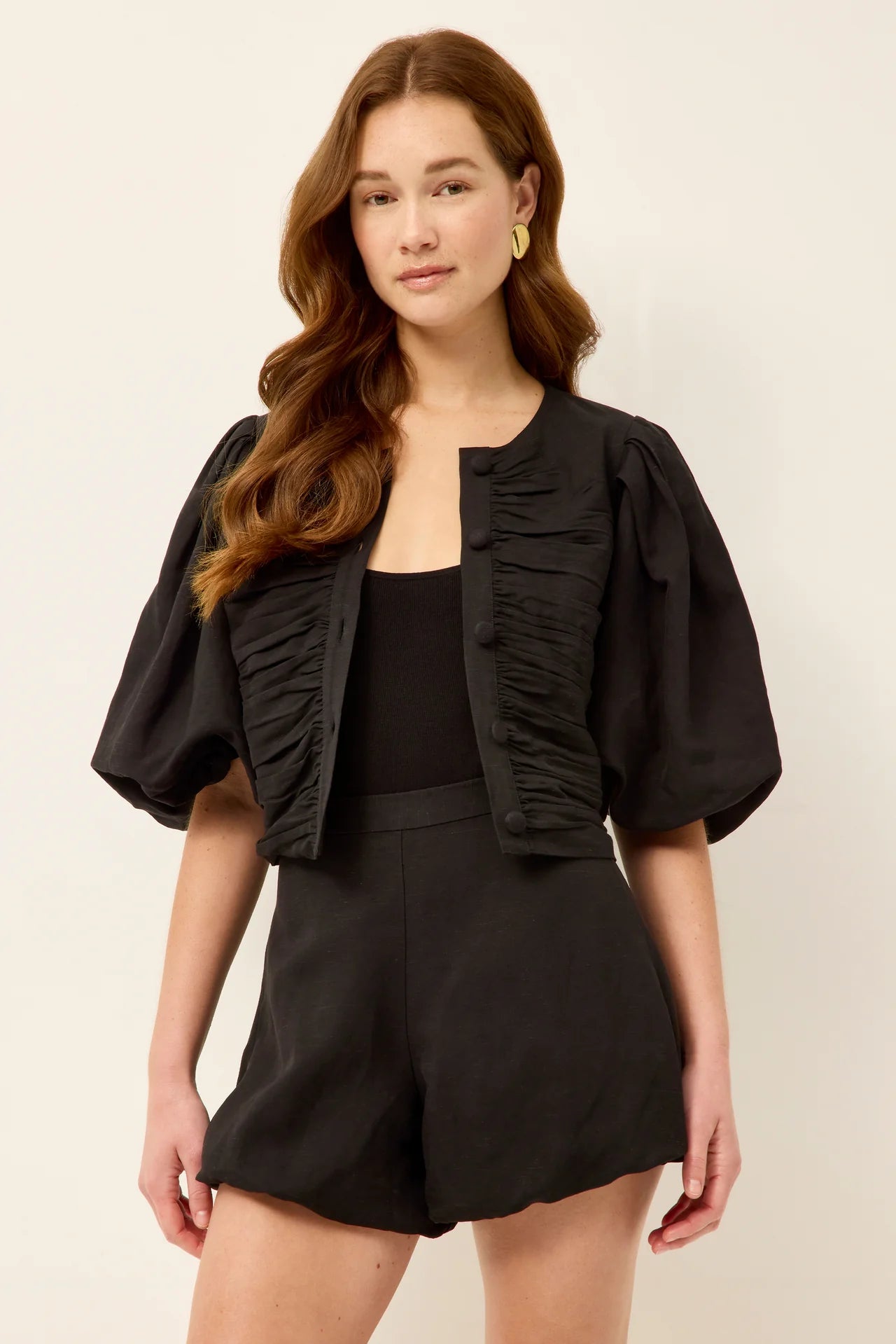 Woman wearing a black ruched top and shorts on a beige background