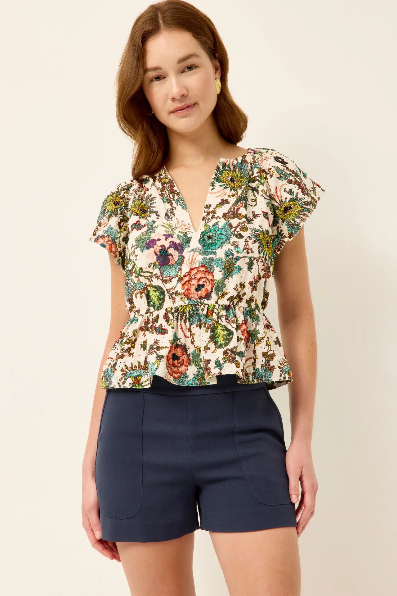 Woman wearing a floral blouse and navy shorts on a beige background