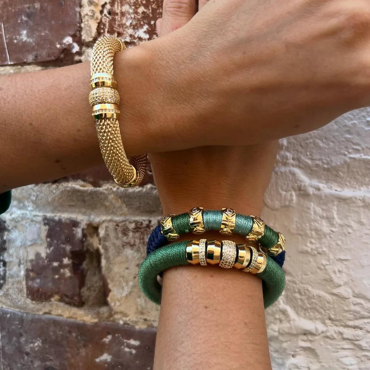 Gold and green bracelets on a wrist against a textured wall background