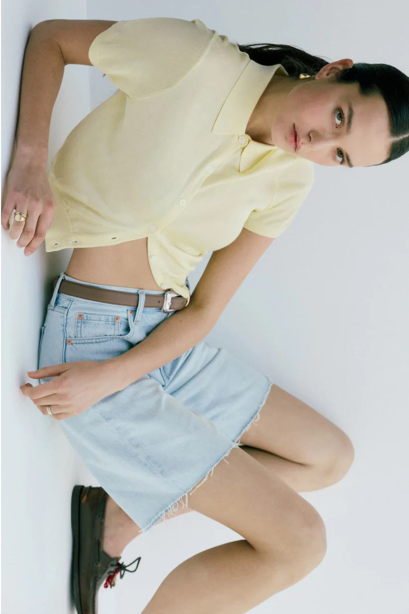 Woman wearing a yellow top and light blue denim skirt on a white background