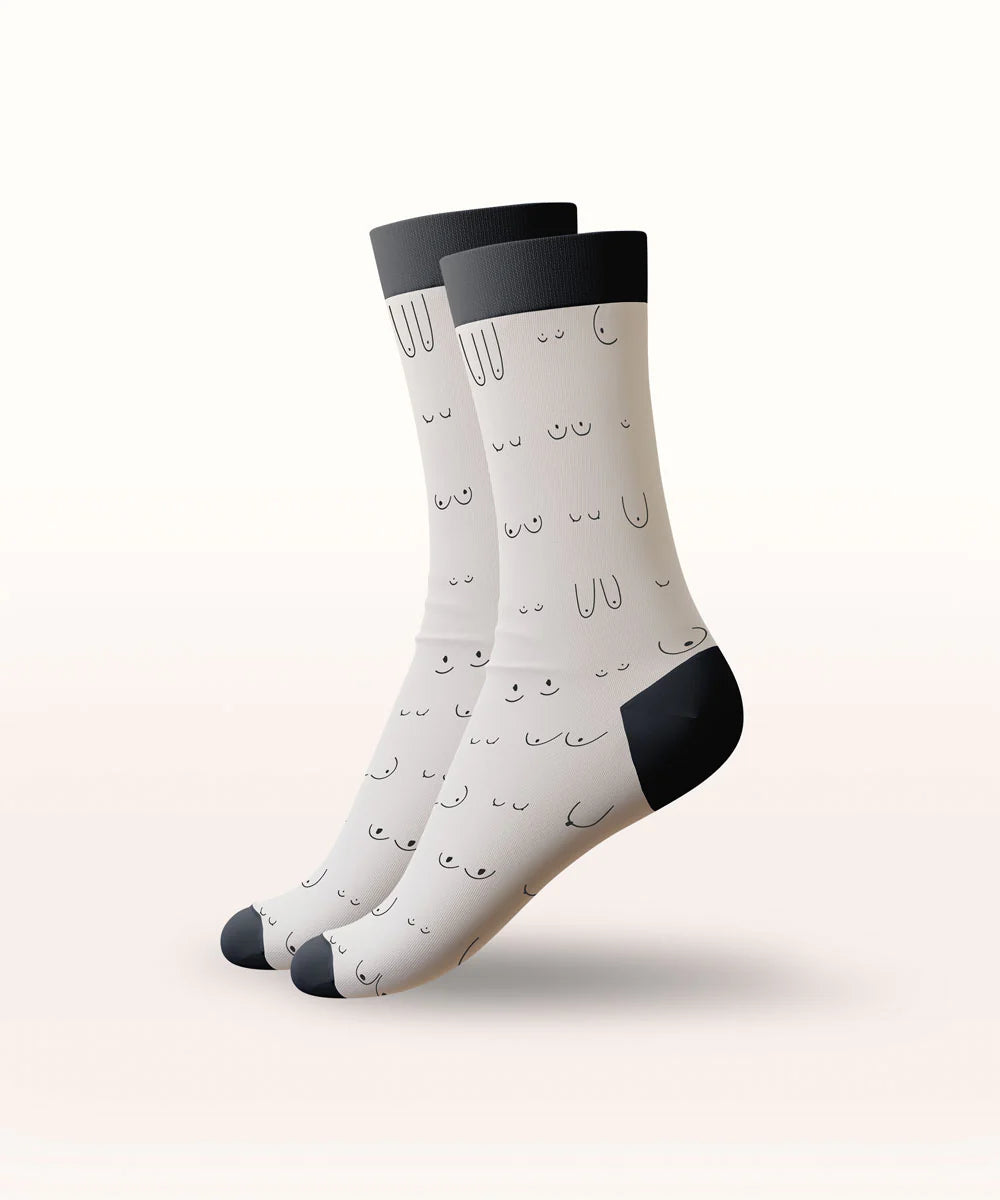 A pair of crew socks with a white base, black cuffs, heels, and toes, and a minimalist black line-art face pattern, shown floating against a light beige gradient background.