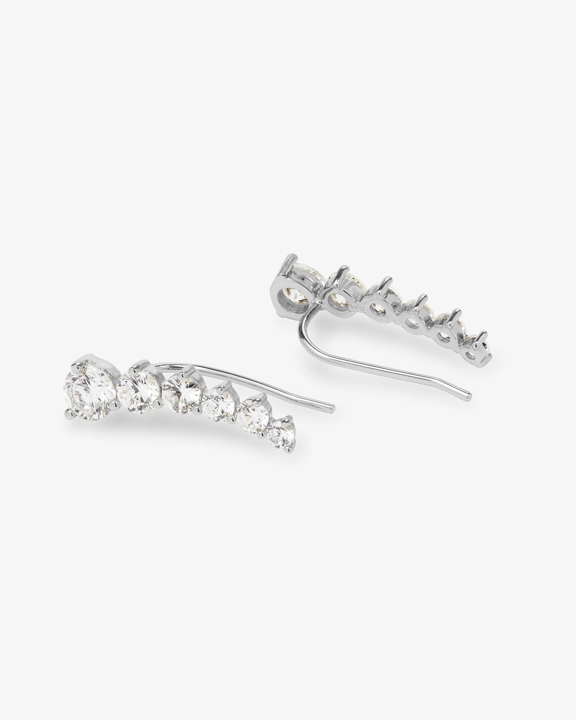 A pair of silver-toned drop earrings with a curved row of clear round-cut stones, shown on a light gray background.