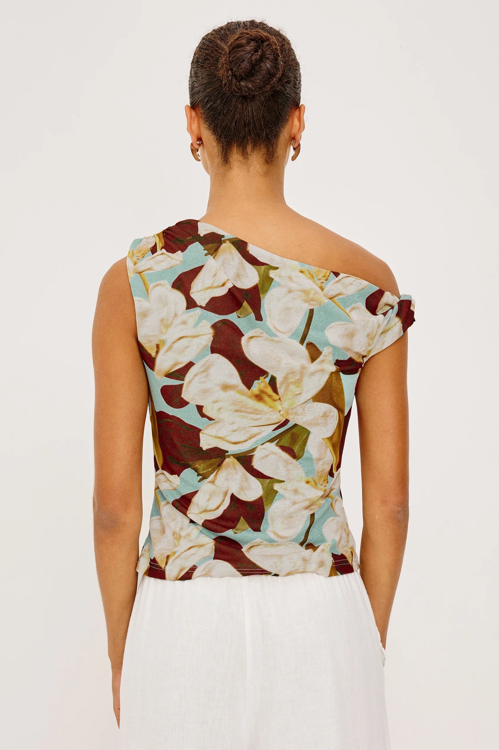 Woman wearing a floral one-shoulder top with a plain background