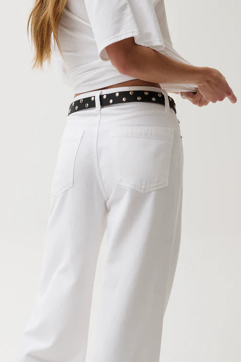 Person wearing white pants with a black belt featuring white studs on a plain background