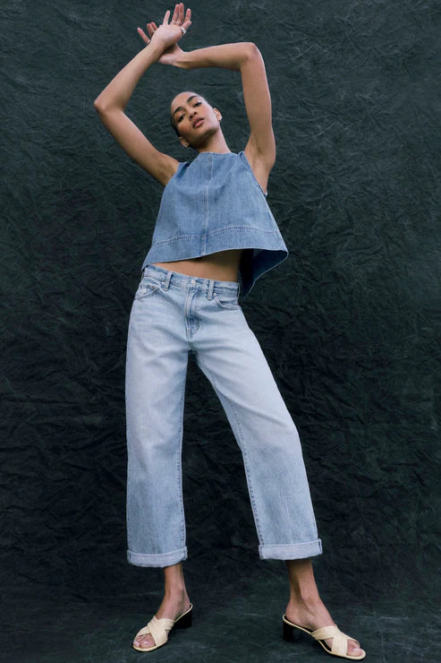 Person wearing a denim crop top and jeans against a dark textured wall