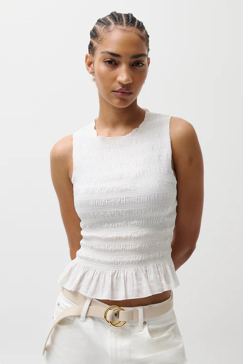 Woman wearing a white sleeveless top with a peplum waist and white pants on a white background