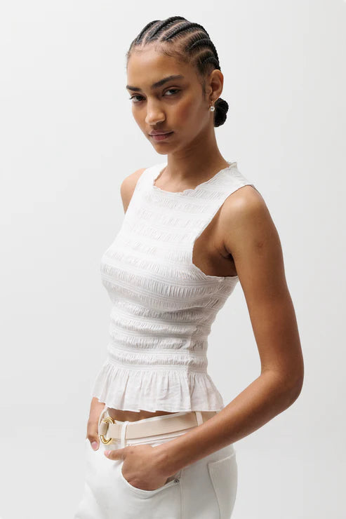 Woman wearing a white sleeveless top against a plain background