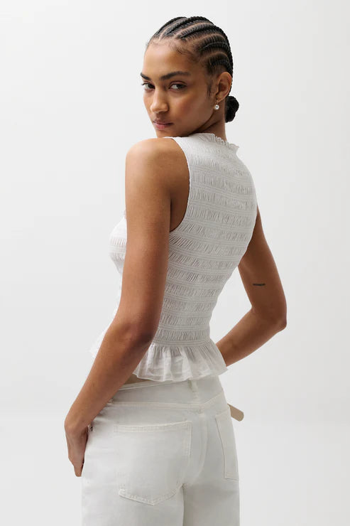 Woman wearing a white sleeveless top and pants on a plain background