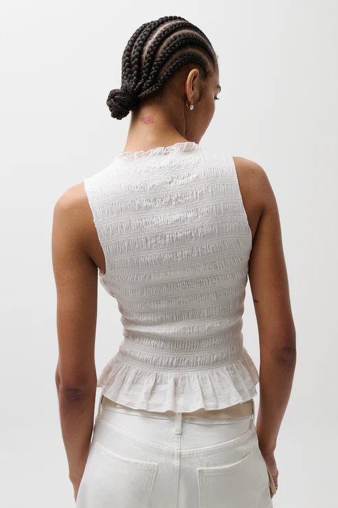 Person wearing a white sleeveless top with ruffled details on a plain background
