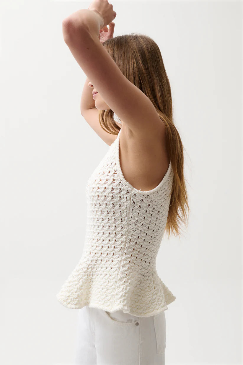 Woman wearing a white crochet top against a plain background