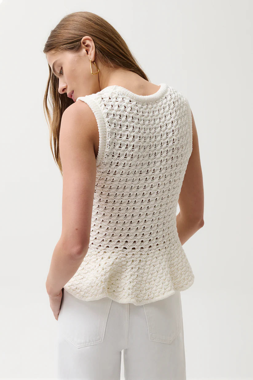 Woman wearing a white crochet sleeveless top against a plain background