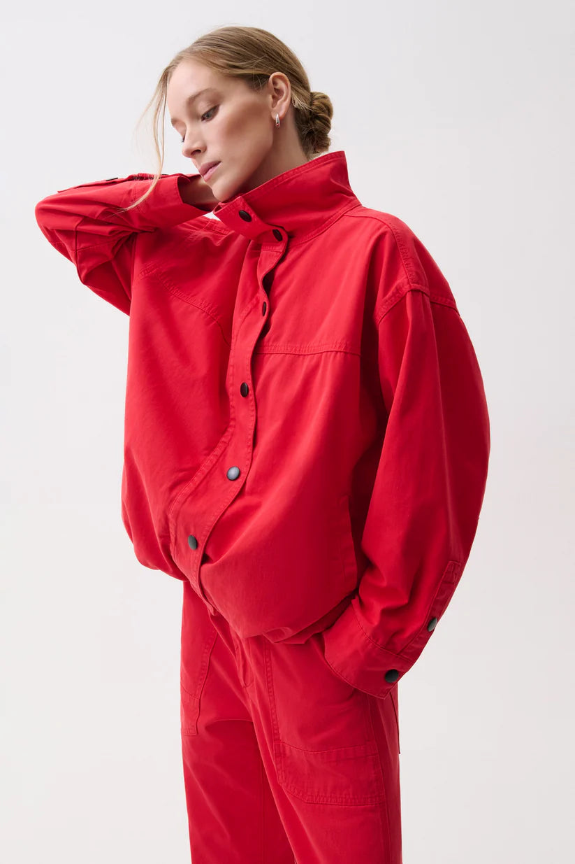 A model wearing a bright red oversized utility jumpsuit with a high collar and button front, posed against a clean light gray studio background.