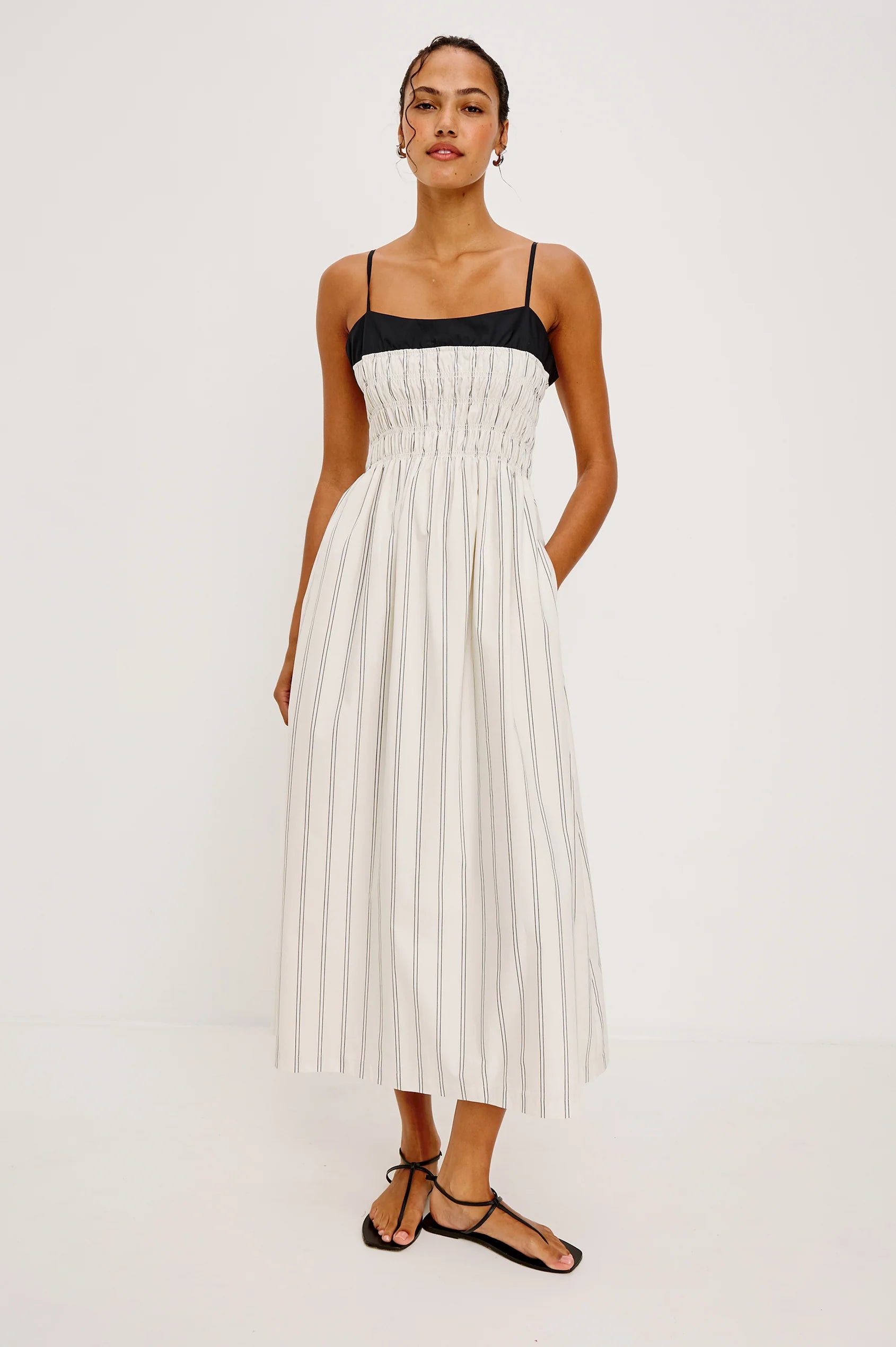 Woman wearing a white pleated dress with a black top on a white background