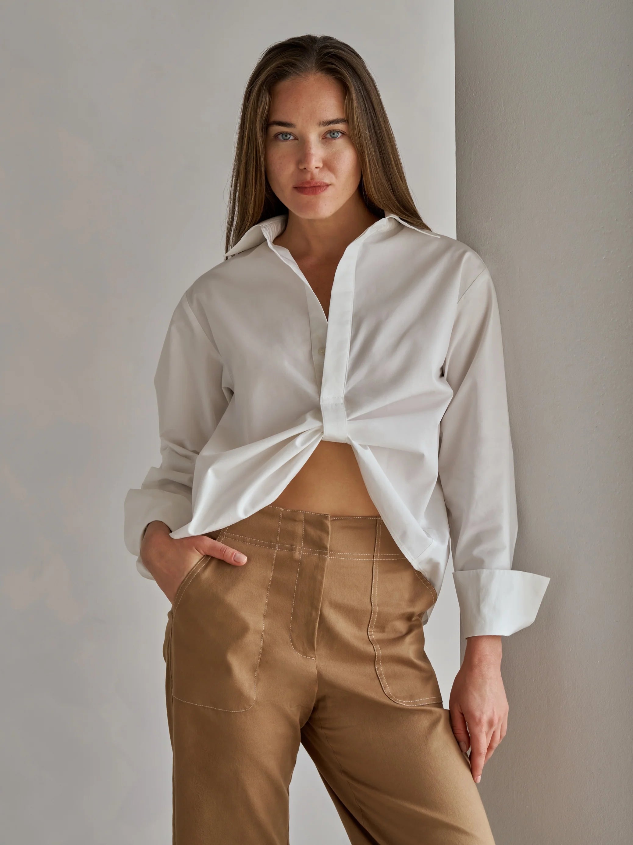 Woman wearing a white shirt and beige pants against a plain background