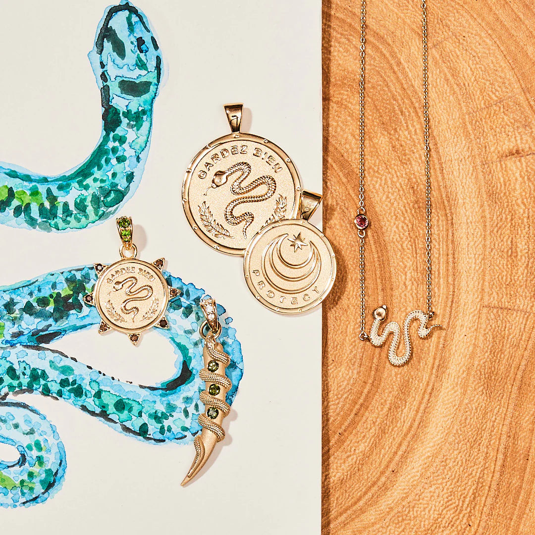 Gold snake-themed jewelry on a wooden surface with a painted snake design.