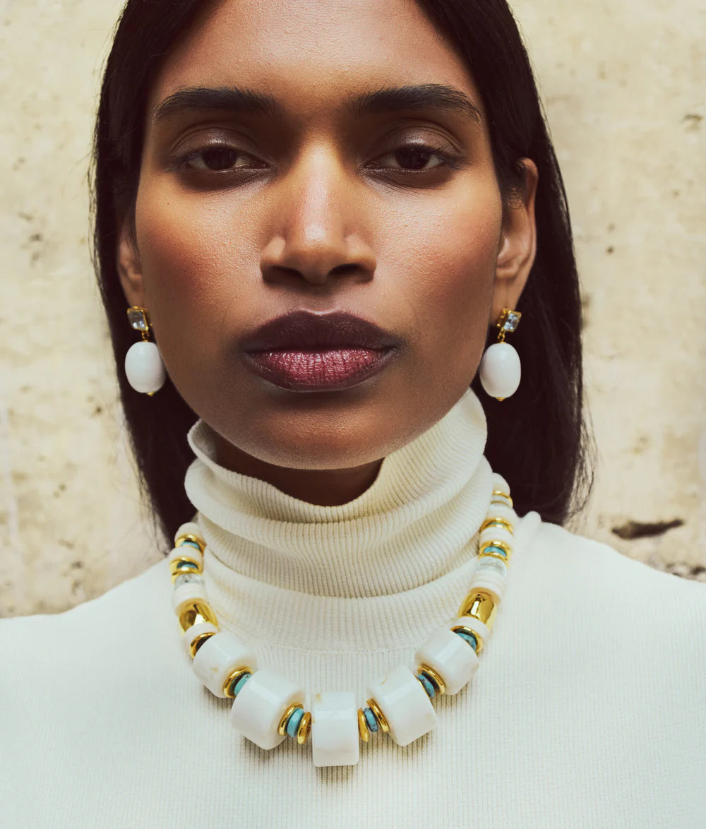 Woman wearing a white turtleneck sweater and a necklace with large white beads and gold accents.