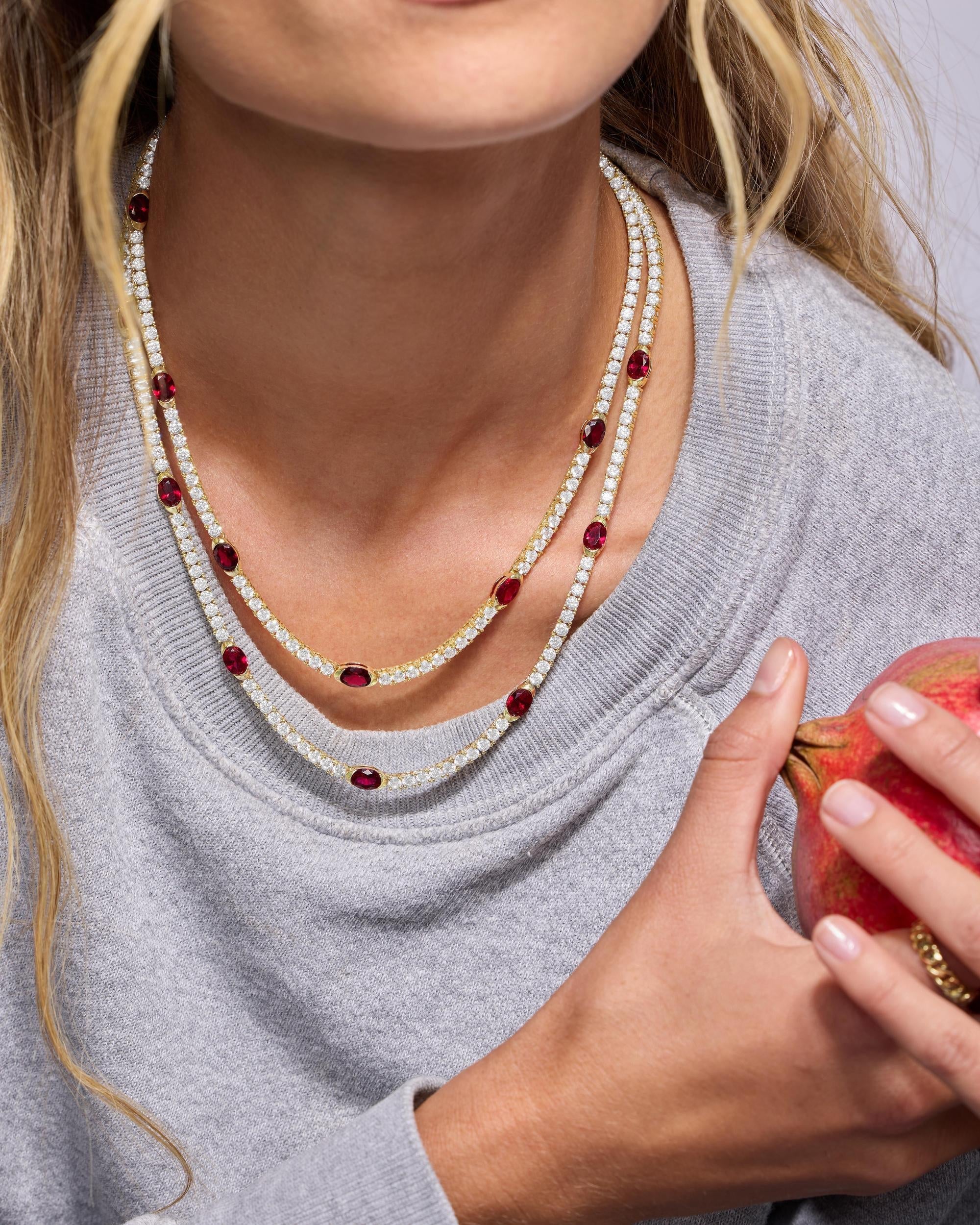 Close-up of a person wearing a layered necklace with red and clear stones, holding a red apple.
