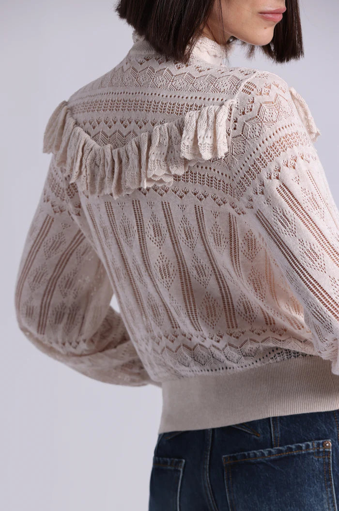 Close-up of a person wearing a beige lace blouse with a plain background