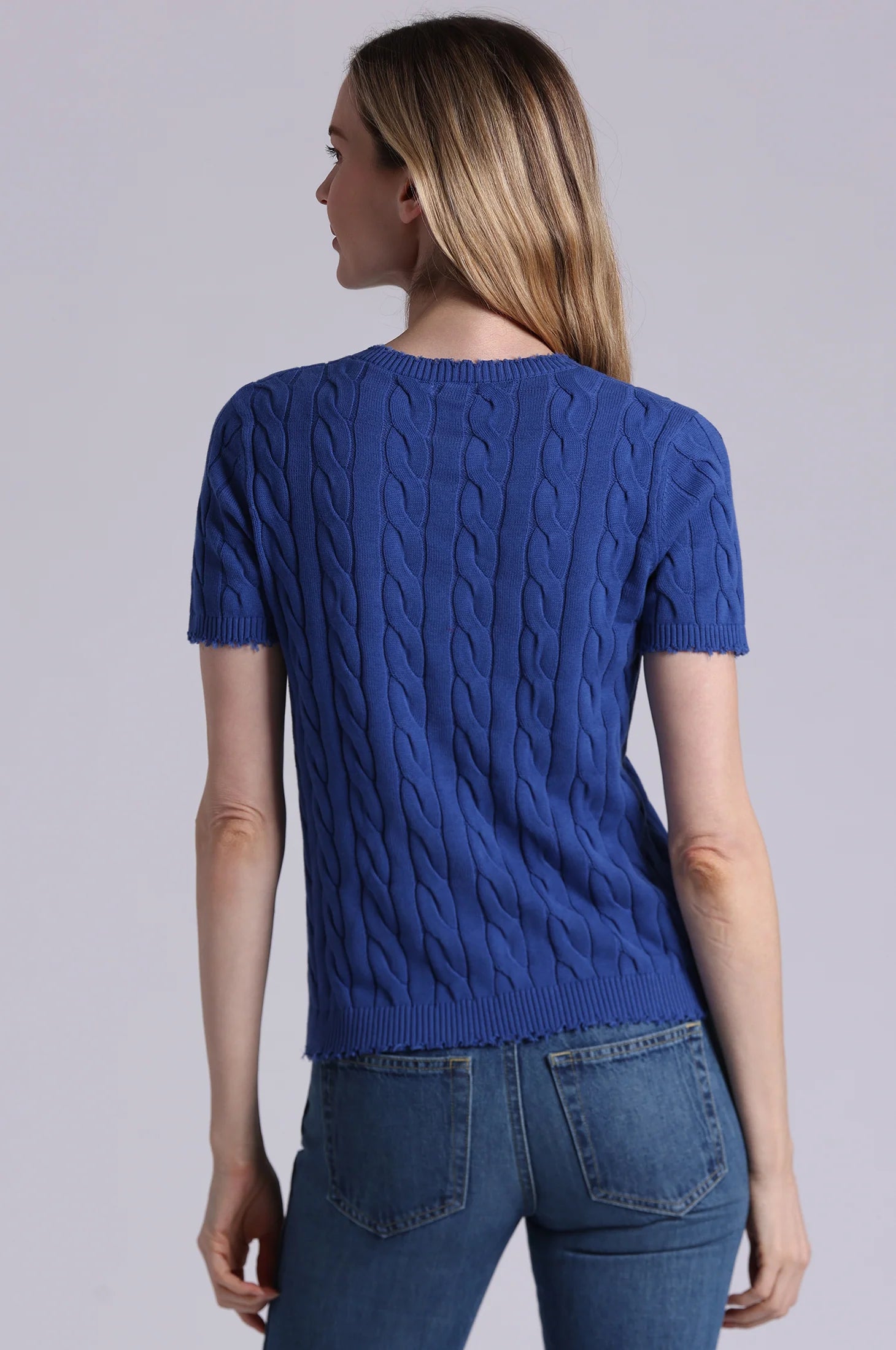 Woman wearing a blue cable knit sweater and jeans on a gray background