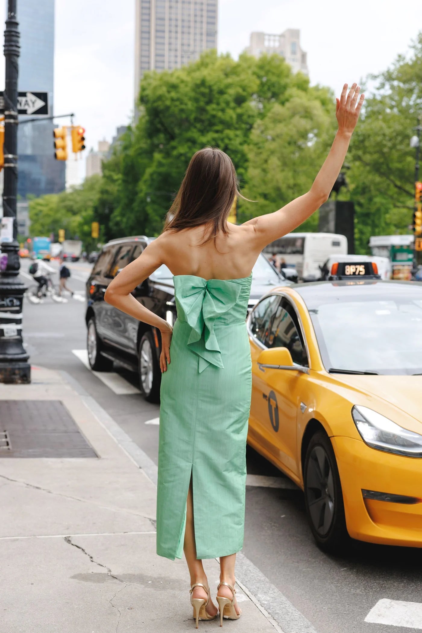 Woman in a green dress waving at a yellow taxi in an urban setting