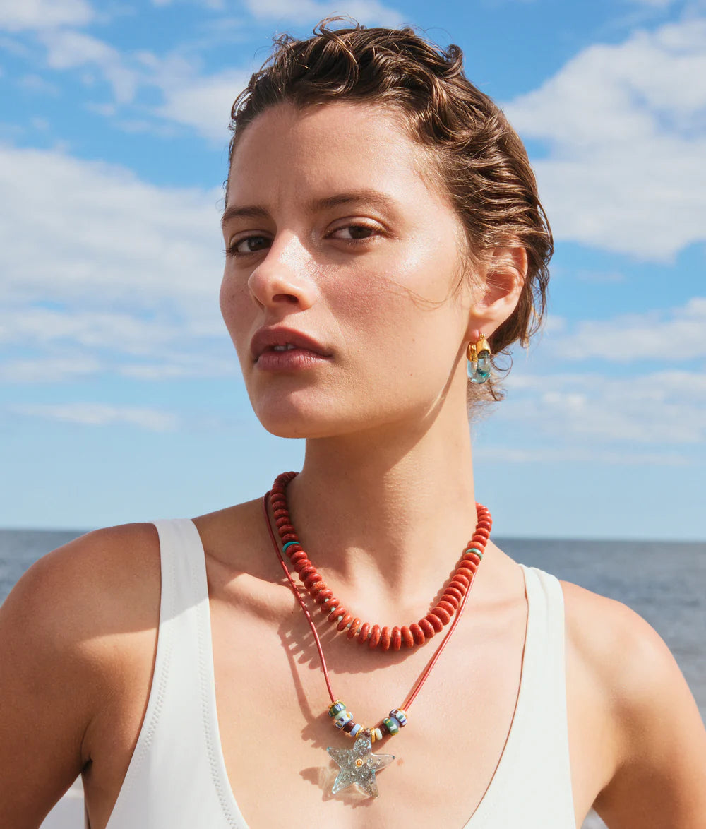 Woman wearing a red necklace with a starfish pendant against a blue sky and ocean background