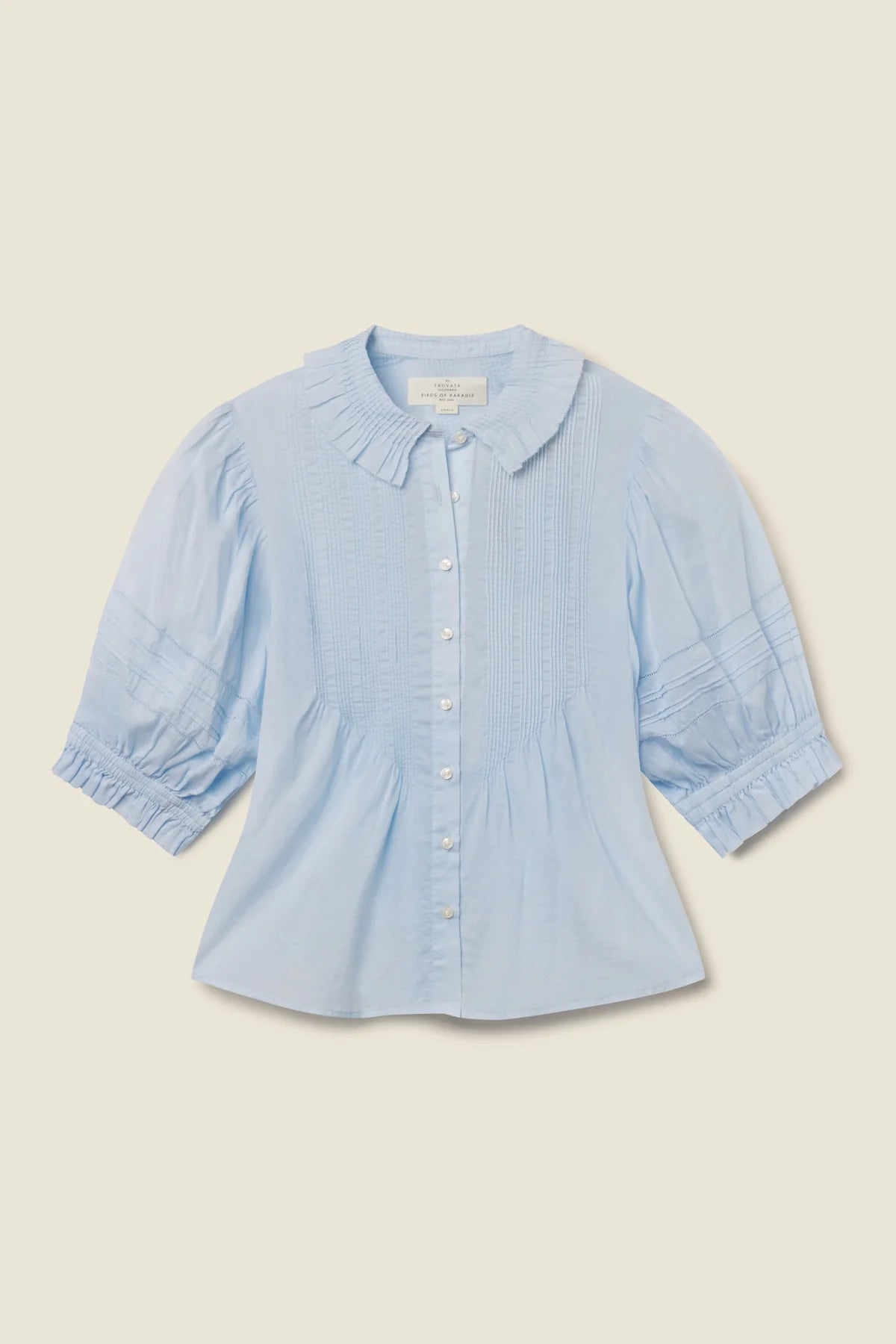 Light blue shirt with ruffled collar on a beige background