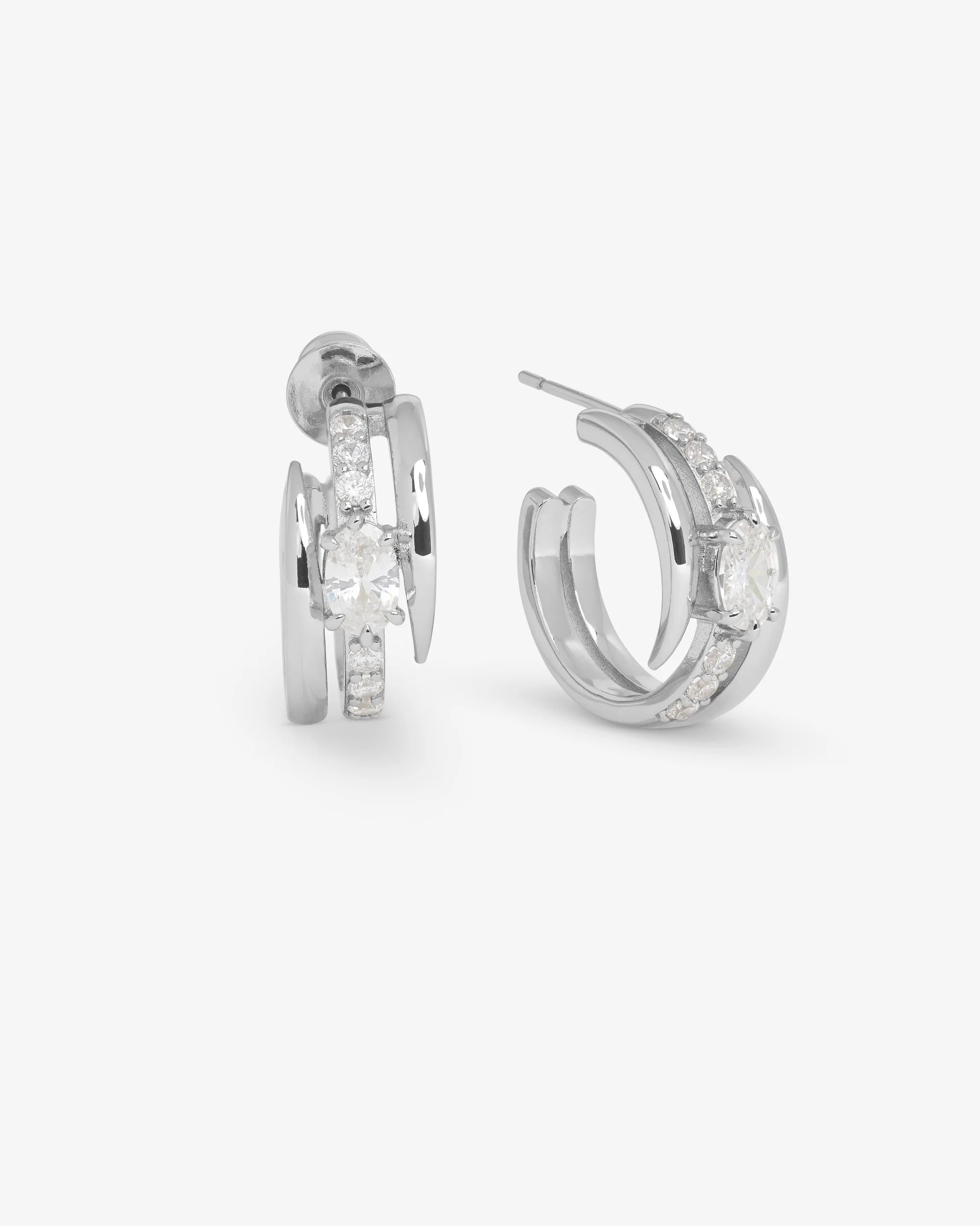 A pair of silver-toned huggie hoop earrings with clear marquise-cut and round stones, shown from side and front angles on a light gray background.