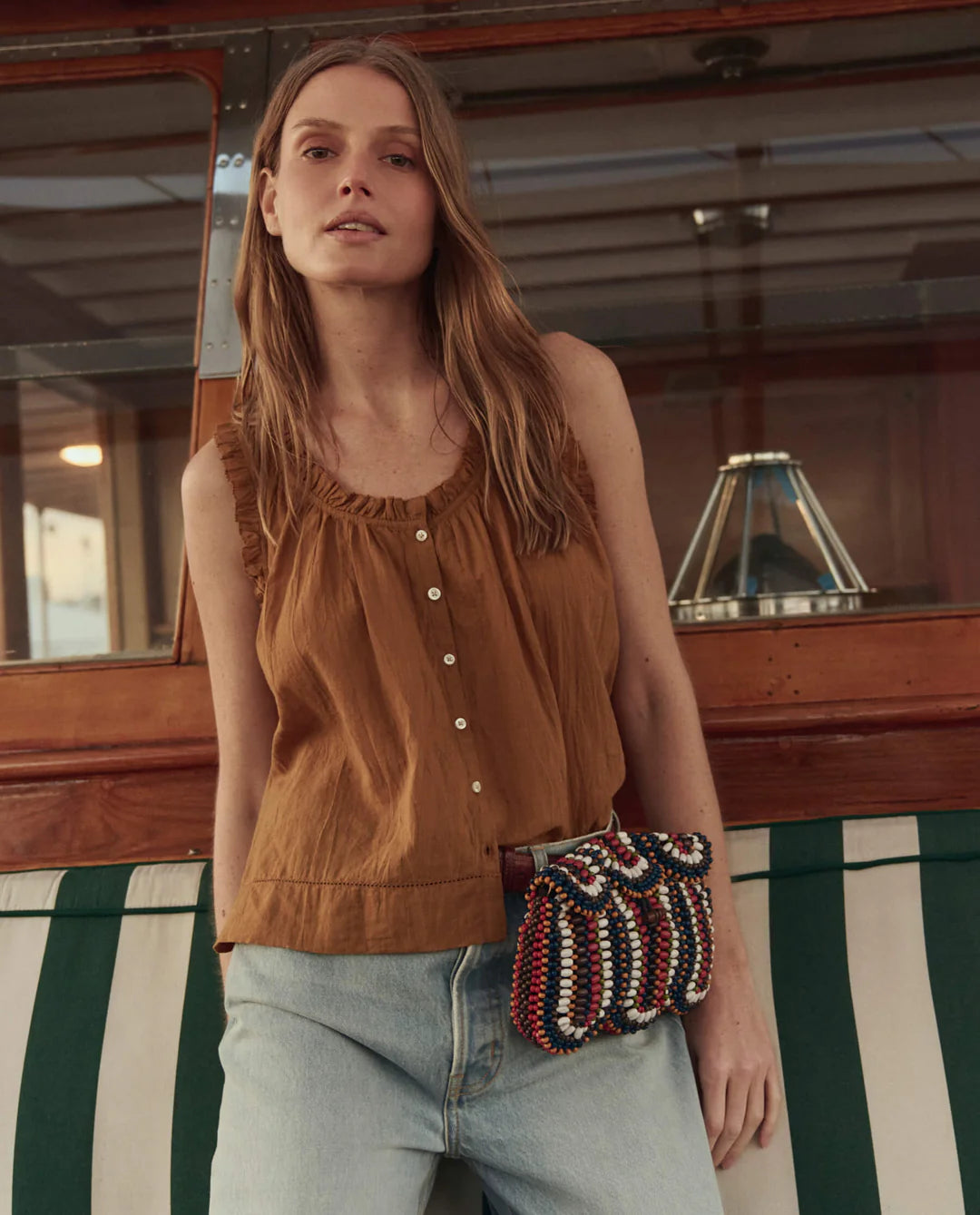 Woman wearing a brown sleeveless top and blue jeans, holding a patterned handbag on a boat.