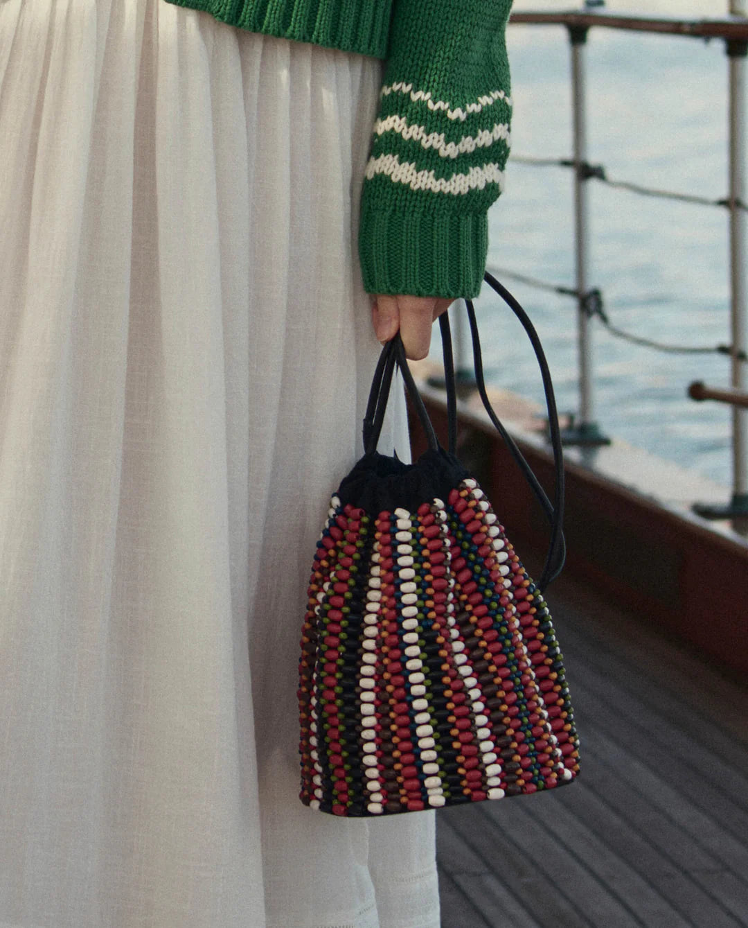 Person holding a multicolored woven bag on a boat deck.