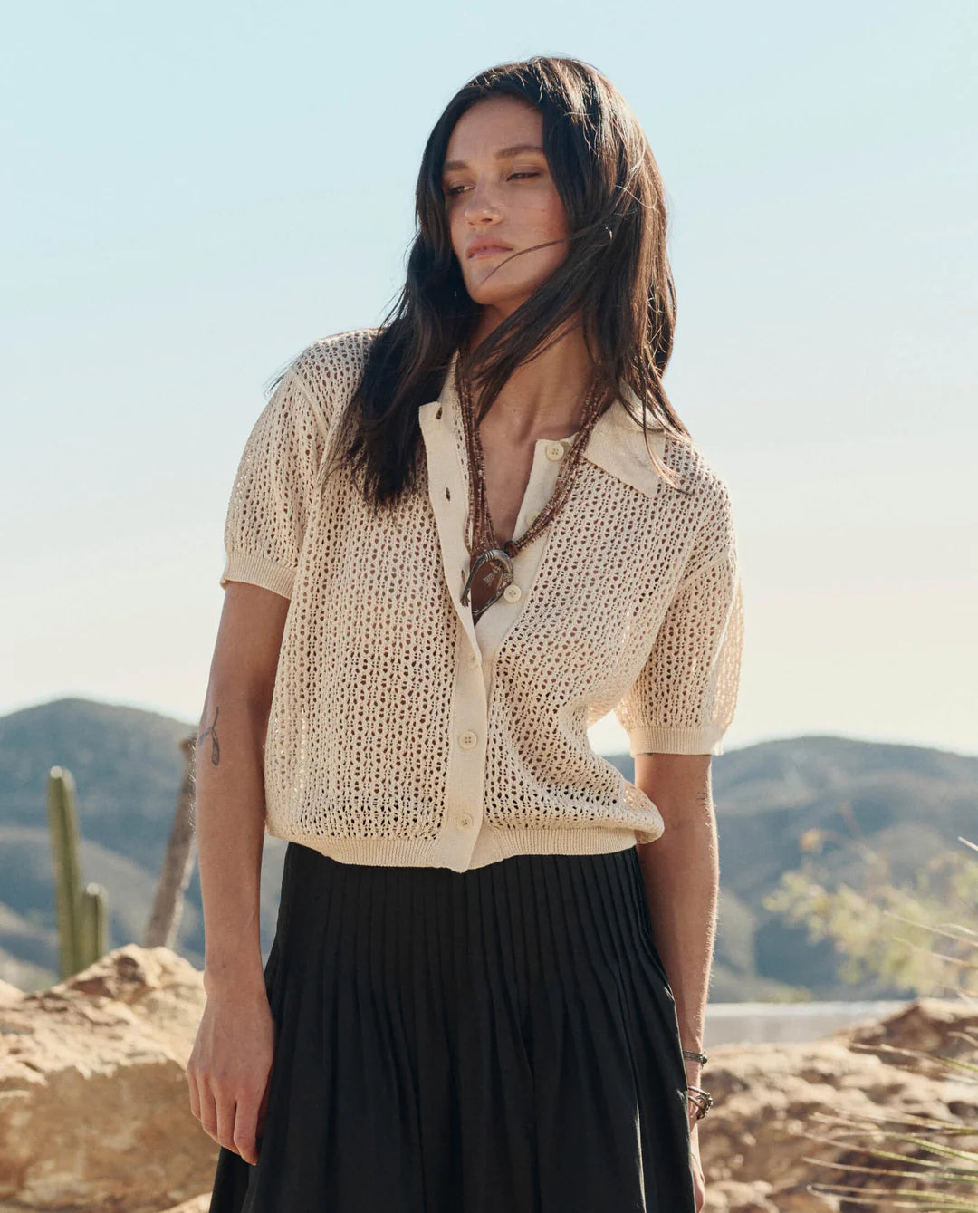 Woman wearing a beige knitted cardigan over a black top with a desert landscape in the background