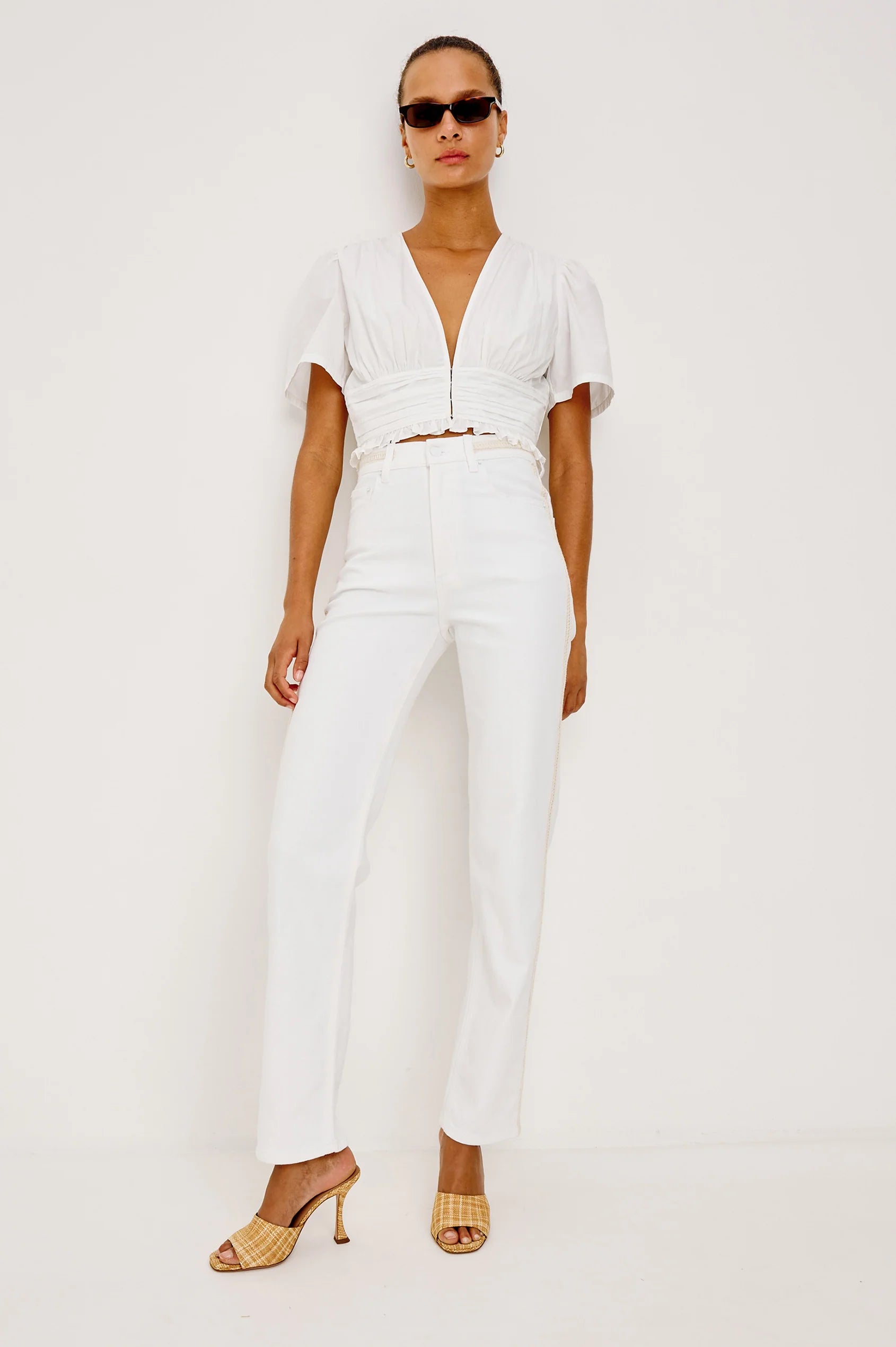 Woman wearing a white outfit with sunglasses on a plain background