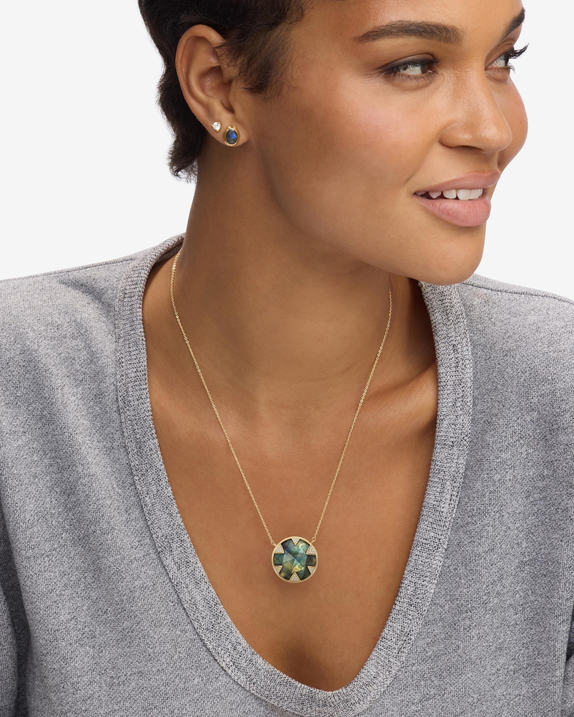 Woman wearing a gold necklace with a green pendant against a neutral background