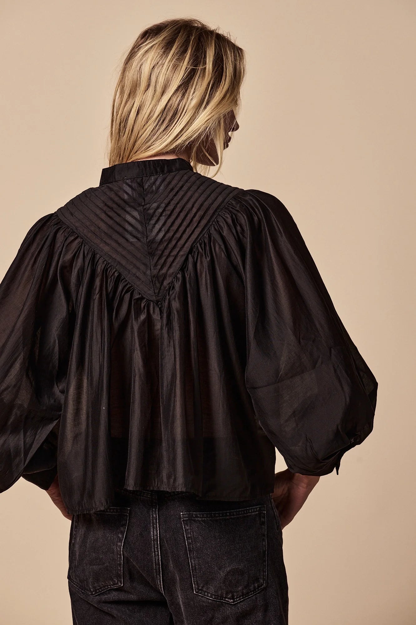 Person wearing a black blouse with puffed sleeves against a beige background