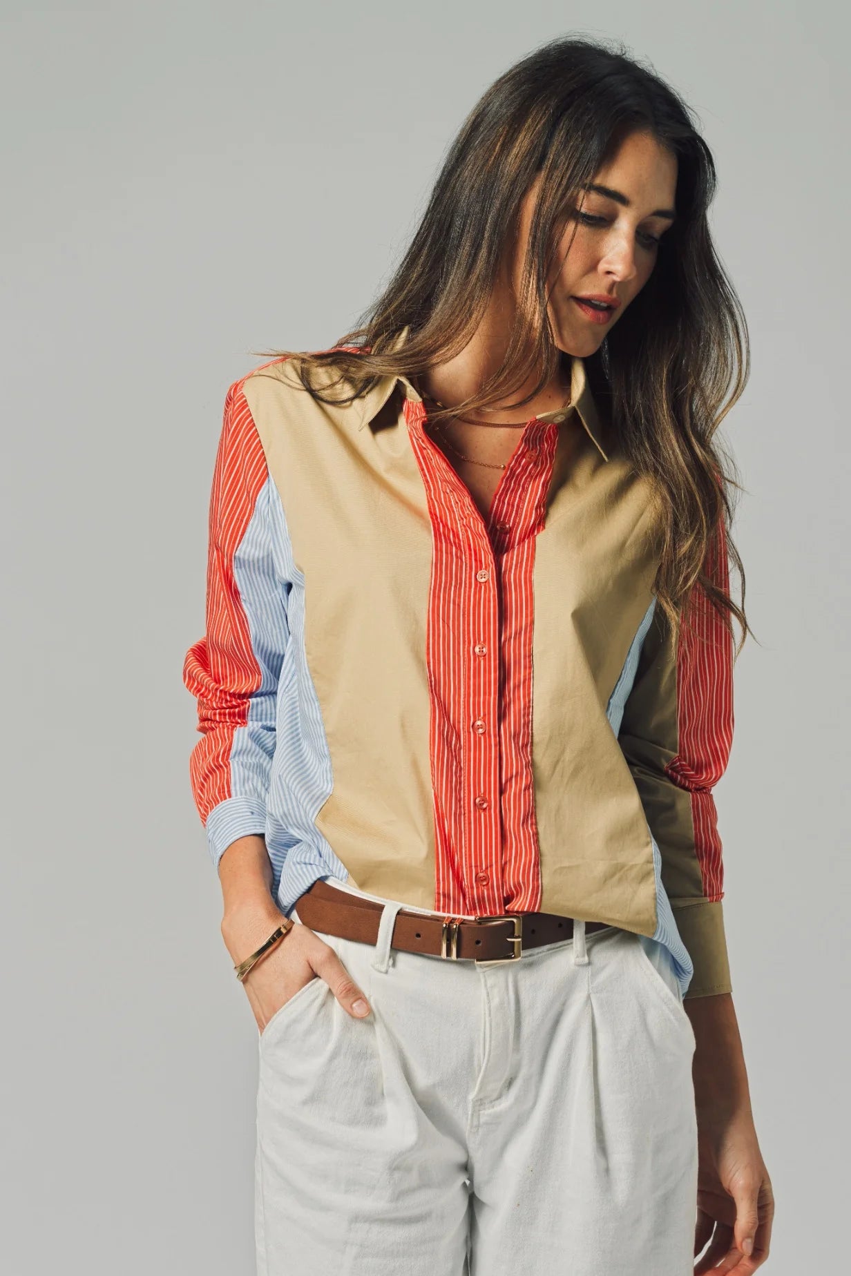 Woman wearing a layered shirt with beige, red, and blue colors on a gray background
