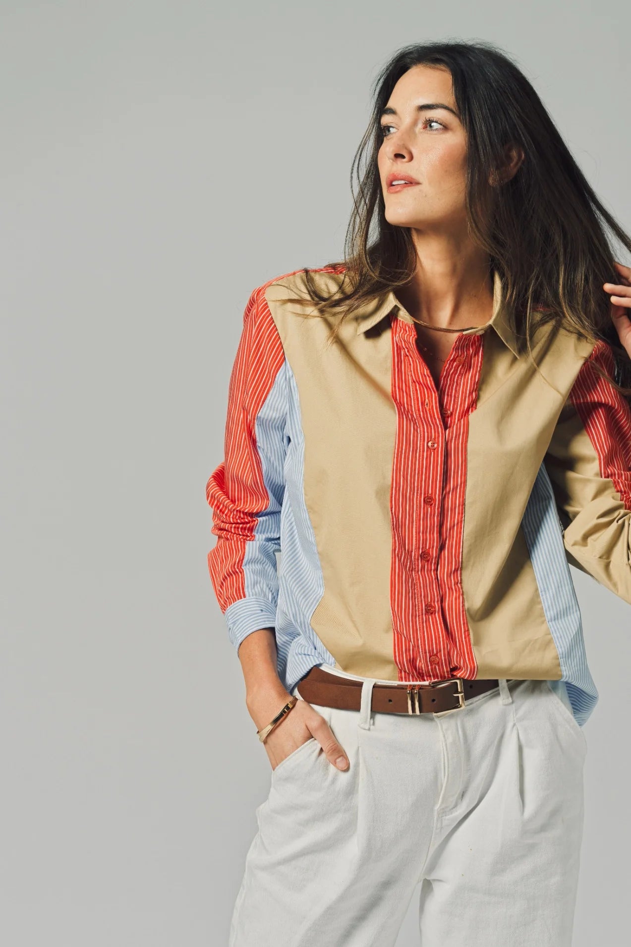 Woman wearing a layered outfit with a beige vest over a red and blue shirt on a gray background