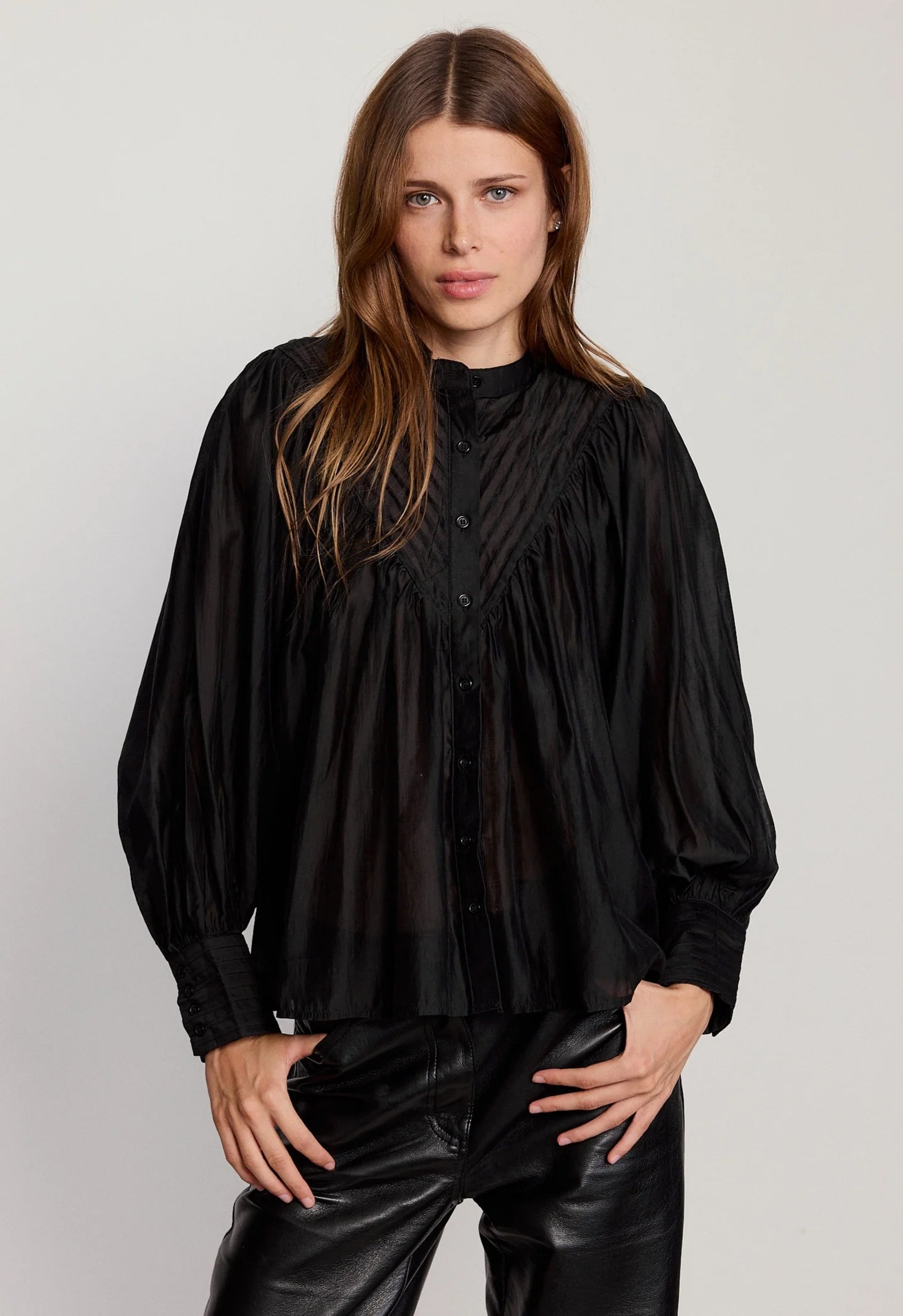 Woman wearing a black blouse and black pants against a plain background