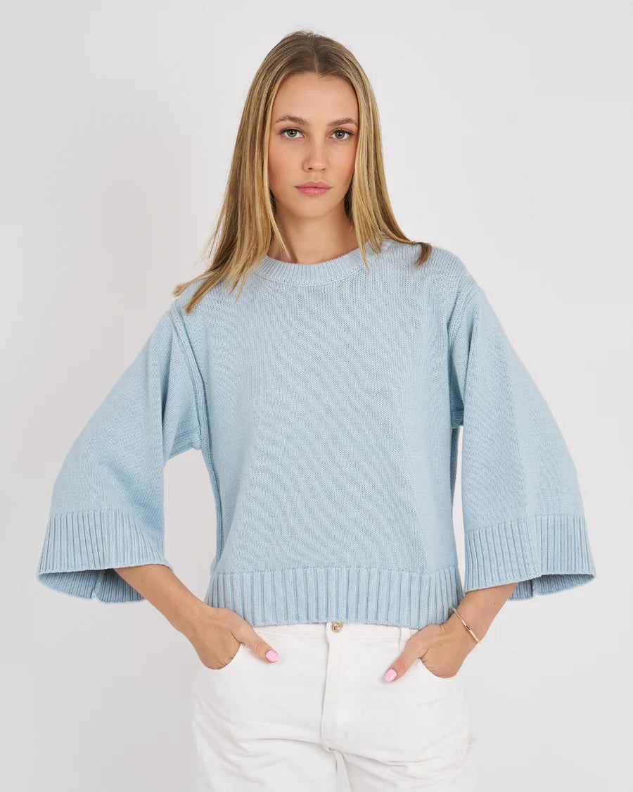 Woman wearing a light blue sweater with wide sleeves on a white background