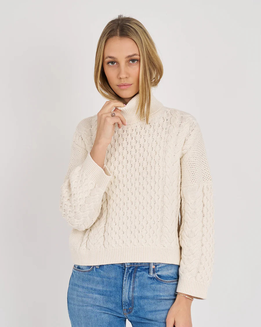 Woman wearing a cream knitted sweater and blue jeans on a white background
