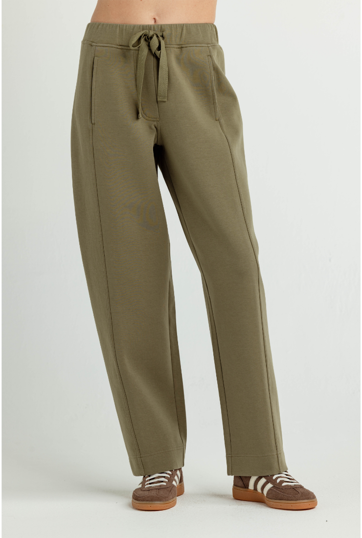 A person wearing olive green drawstring sweatpants with side pockets, paired with brown sneakers, shown from the waist down against a light gray studio background.