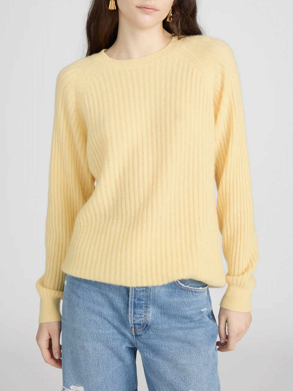 Person wearing a yellow ribbed sweater and blue jeans on a plain background